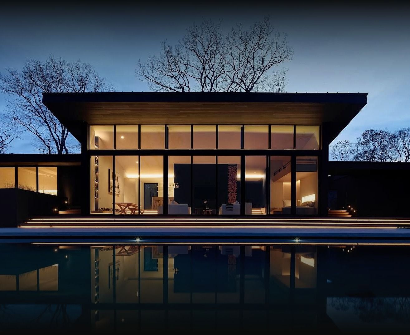 Modern Hamptons residence lit at dusk, reflected in the pool